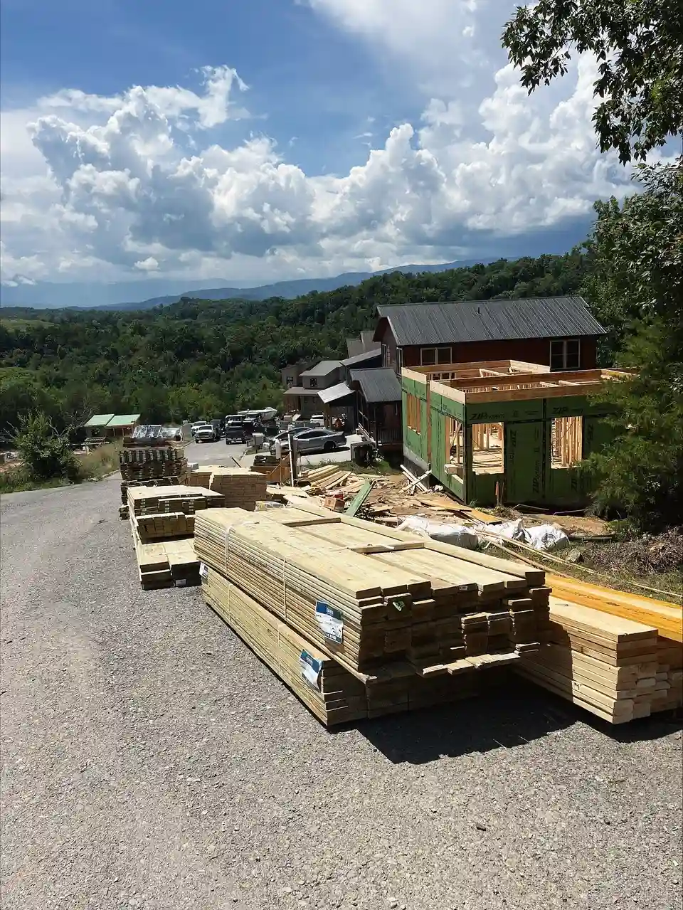 Vendor Price Sourcing: lumber packs staged along a gravel drive at a mountain job site